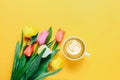 Cup of coffee and beautiful tulips on yellow background, top view Royalty Free Stock Photo