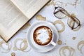 A cup of coffee beverage, reading glasses and a paper old book on a white table with coffee stains Royalty Free Stock Photo