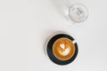 Cup of coffee on black saucer and glass of water on white background. Fresh cappuccino with beautiful latte art in shape Royalty Free Stock Photo