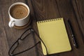 Cup of coffee, blank notepad, pen and glasses on wooden table Royalty Free Stock Photo