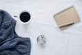 Cup coffee , blue knitted sweater, notebook with pen, clock, candle on bed, top view