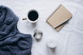 Cup coffee , blue knitted sweater, notebook with pen, clock, candle on bed, top view