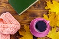 Cup of coffee, book, knitted scarf and yellow maple leaves on wooden table. Autumn still life