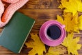 Cup of coffee, book, knitted scarf and yellow maple leaves on wooden table. Autumn still life