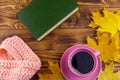 Cup of coffee, book, knitted scarf and yellow maple leaves on wooden table. Autumn still life