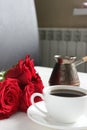 A Cup of coffee and a bouquet of red roses on the table close-up. Royalty Free Stock Photo