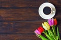 A cup of coffee, a bouquet of tulips on a dark wooden table