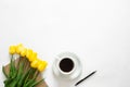 A cup of coffee, bouquet of yellow tulips and a notebook on a white background.
