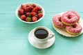 Cup of coffee, bowl with fresh strawberries and white plate with pink donuts on turquoise painted wooden table, top view Royalty Free Stock Photo