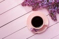 Cup of coffee and branches of blooming lilac on pink wooden table
