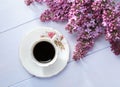 Cup of coffee and branches of blooming lilac on wooden table