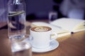 Cup of coffee cappuccino, glass of pure water, bottle on wooden table, bright interior daylight Royalty Free Stock Photo