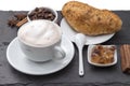 Cup of coffee cappuccino with milk foam on a saucer, fresh baked bun, caramelized sugar, coffee beans, cinnamon. Popular Royalty Free Stock Photo