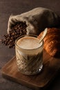 Cup of coffee cappuccino in transparent glass with french fresh croissant, Roasted coffee beans in a bag scattered on a table Royalty Free Stock Photo