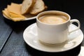 A cup of coffee with cheese and bread on black wooden table