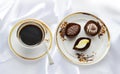 A cup of coffee and chocolate candies in a delicious plate on a white silk background Royalty Free Stock Photo