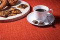 Cup of coffee with chocolate on the side. Crispy brown baked biscuits with black sesame seeds on wooden board. Bright red textile