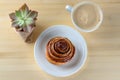 Cup Of Coffee, Cinnamon Roll Bun Pastry Danish Swirl And Small Succulent Plant Over The Wood Background.