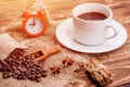 Cup of coffee with  cinnamon sticks, anise, coffee beans and red alarm clock on wooden background Royalty Free Stock Photo