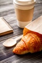 Cup coffee and croissant in paper bag on wooden background Royalty Free Stock Photo