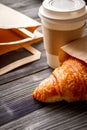 Cup coffee and croissant in paper bag on wooden background