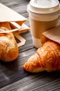 Cup coffee and croissant in paper bag on wooden background Royalty Free Stock Photo