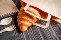 Cup coffee and croissant in paper bag on wooden background Royalty Free Stock Photo