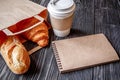 Cup coffee and croissant in paper bag on wooden background Royalty Free Stock Photo