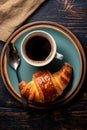 cup of coffee and croissant with spoon on blue plate