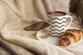 Cup of coffee with croissant on a white plate, with warm blanket. Breakfast, selective focus, toned.