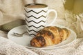 Cup of coffee with croissant on a white plate, with warm blanket. Breakfast, selective focus, toned.