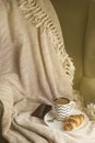 Cup of coffee with croissant on a white plate, with warm blanket. Breakfast, selective focus, toned. Vertical image, copy space.