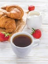 Cup of coffee, croissants, strawberry and milk jar