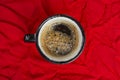 Cup of coffee on crumpled red cloth top view close-up