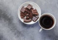 Cup of coffee and dark chocolate on white plate on grey background, top view