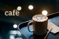 A cup of coffee with design pattern in a white cup on tray and and text cafe in dark background, soft focus Royalty Free Stock Photo