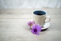 Cup of coffee with flowers. Morning coffee concept with soft purple orchid daisy flower on white table bright background.