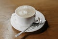 A cup of coffee with foam on a napkin with a spoon in a white saucer on a wooden table background Royalty Free Stock Photo