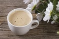 Cup of coffee with foam on a wooden background with a bouquet of large daisies