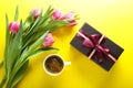 Cup of coffee, gift box and pink tulips on yellow background, to Royalty Free Stock Photo