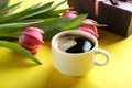 Cup of coffee with gift box and tulips bouquet on yellow background, close up Royalty Free Stock Photo
