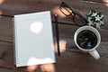 Cup of coffee, glasses, notebook paper, pencil and white flowers on wood background Royalty Free Stock Photo