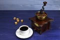 A cup of coffee and coffee grinder on a blue wooden background. White coffee cup and saucer. Copy space. Place for text Royalty Free Stock Photo