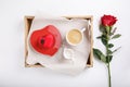 Cup of coffee and heart shaped pink cake on wooden tray. Festive breakfast and red rose on white table. Top view.  Copy space. Royalty Free Stock Photo