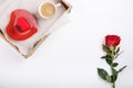 Cup of coffee and heart shaped pink cake on wooden tray. Festive breakfast and red rose on white table. Top view.  Copy space. Royalty Free Stock Photo