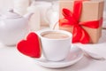 Cup of coffee and a heart shaped red cookie with gift box and teapot on the white table Royalty Free Stock Photo