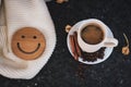 A cup of coffee is the key to a good mood. Wooden smiley on a dark, black, textural background. On the table there is a white, Royalty Free Stock Photo