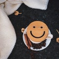 A cup of coffee is the key to a good mood. Wooden smiley on a dark, black, textural background. On the table there is a white, Royalty Free Stock Photo