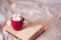 Cup of coffee with knitted red cloth staying on open paper bookin bed closeup over glowing lights. Winter holiday season. Cozy Royalty Free Stock Photo