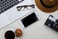 Cup of coffee, laptop, eyeglasses, smartphone, camera and hat on